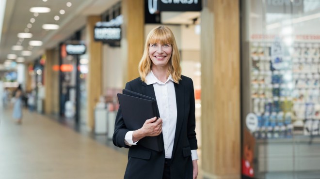 Une collaboratrice du service immobilier devant les magasins de détail d'un mégastore Coop.