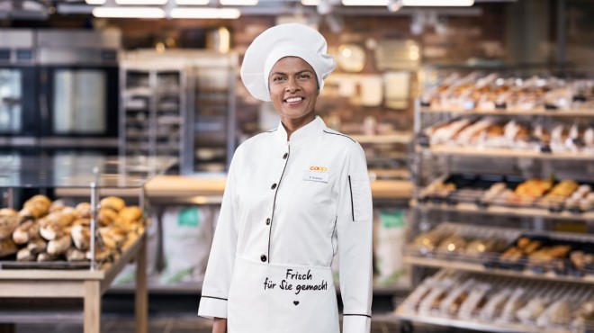 Una panettiera sorride all'obiettivo di fronte al reparto Panetteria di un supermercato Coop.