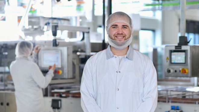 Un uomo sorride alla telecamera davanti a una pianta 